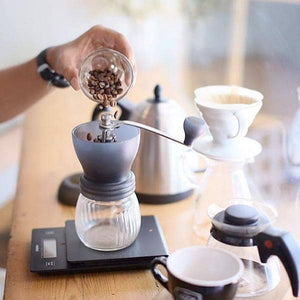 Man making coffee with a Hario coffee grinder, Hario V60, Hario V60 scale/timer, and Bonavita kettle